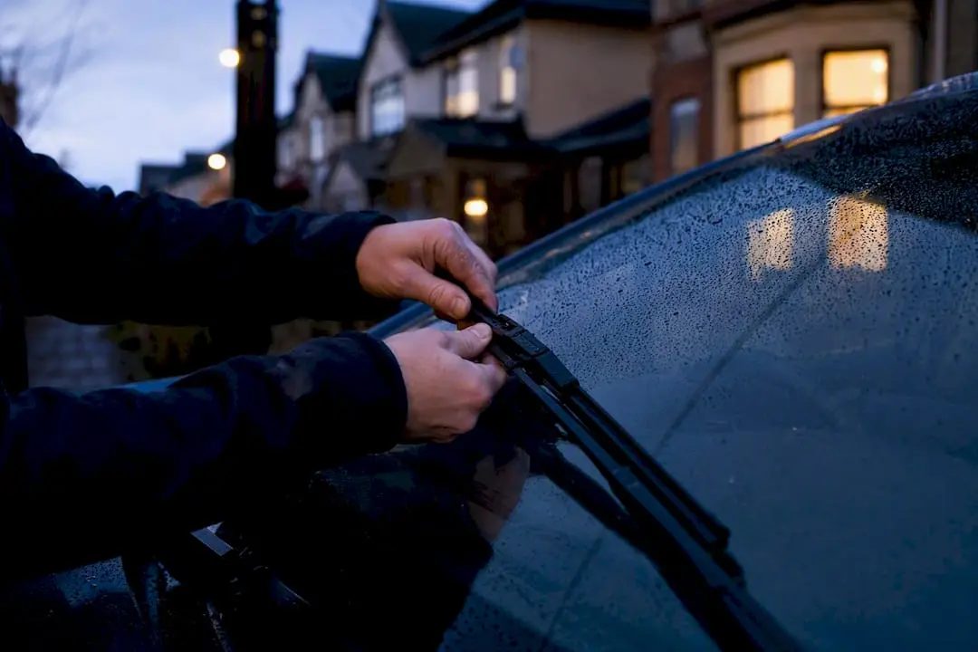 Hands fitting windshield wiper on wet windscreen